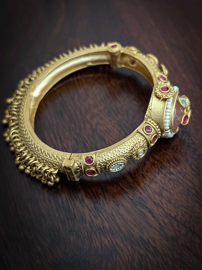 Oval coloured stone in center of single openable kada with kundan studded inlay work on stone and ghunghru hangings